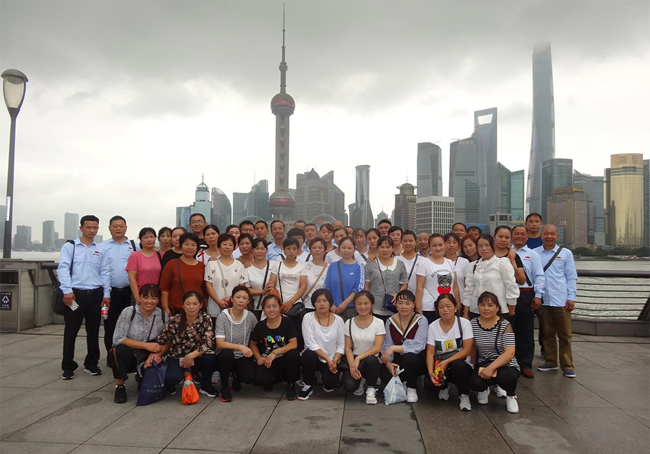 Yuminaga employees posing for a group photograph on The Bund in Shanghai during a five-day company trip in 2010, with the Pudong skyline behind them.